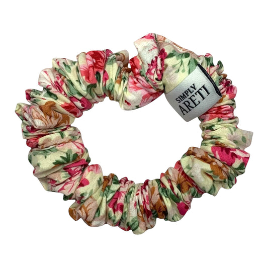 Floral patterned XS scrunchie light beige with a brand label on a white background, 
scrunchie σε XS μέγεθος υφασμάτινο σε χρώμα μπεζ με παστέλ λουλούδια ιδανικό για καθημερινή χρήση. 